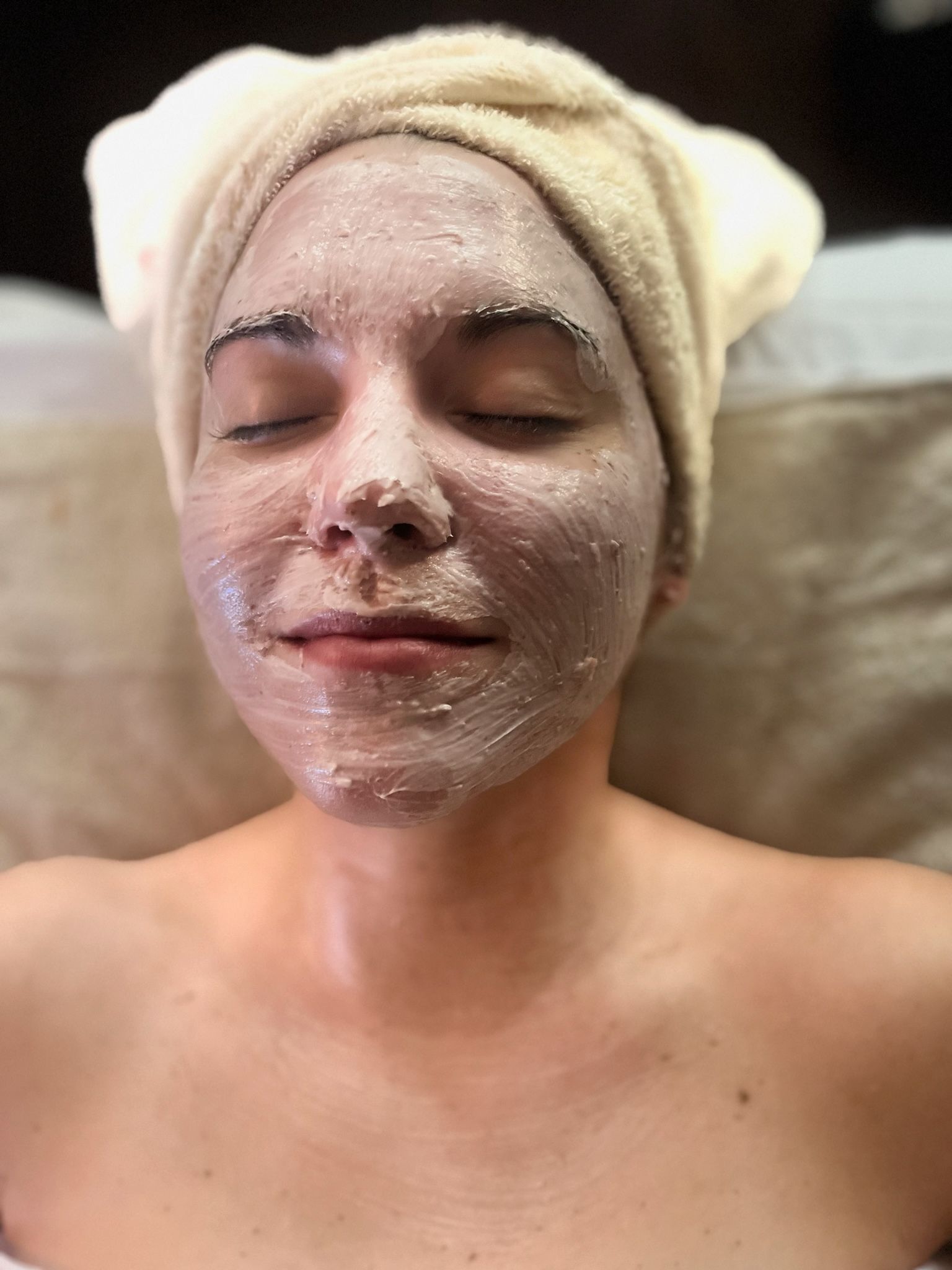 A woman is getting a white mask on her face at a spa.