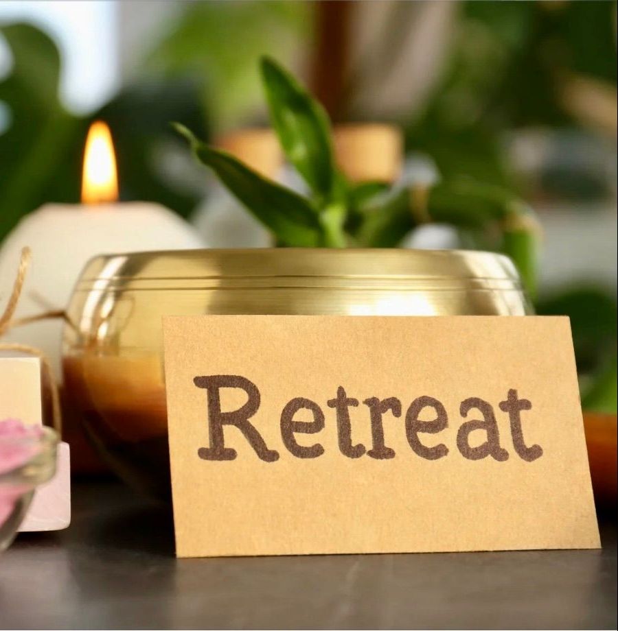 Tan sign that says Retreat leaning against a golden bowl with candle and plants on a table.