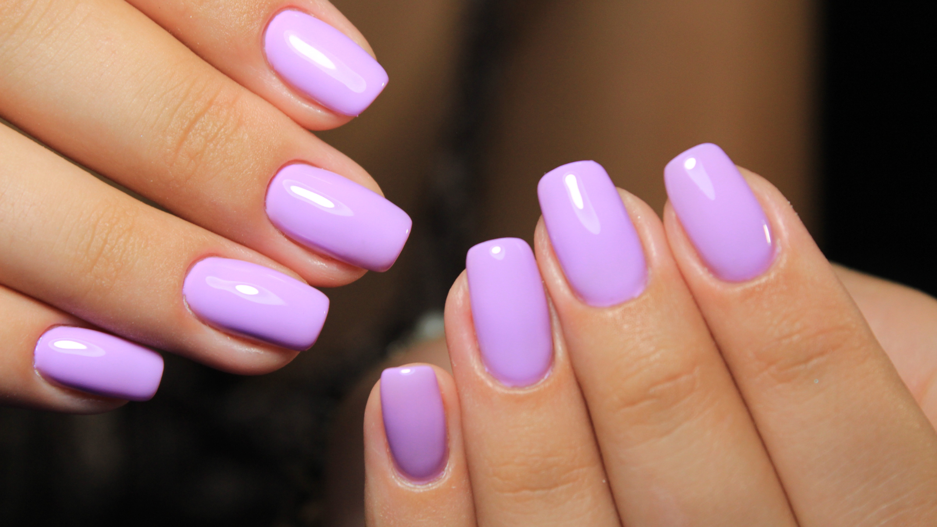 A woman 's hand with pink nail polish and pearls on a pink background.