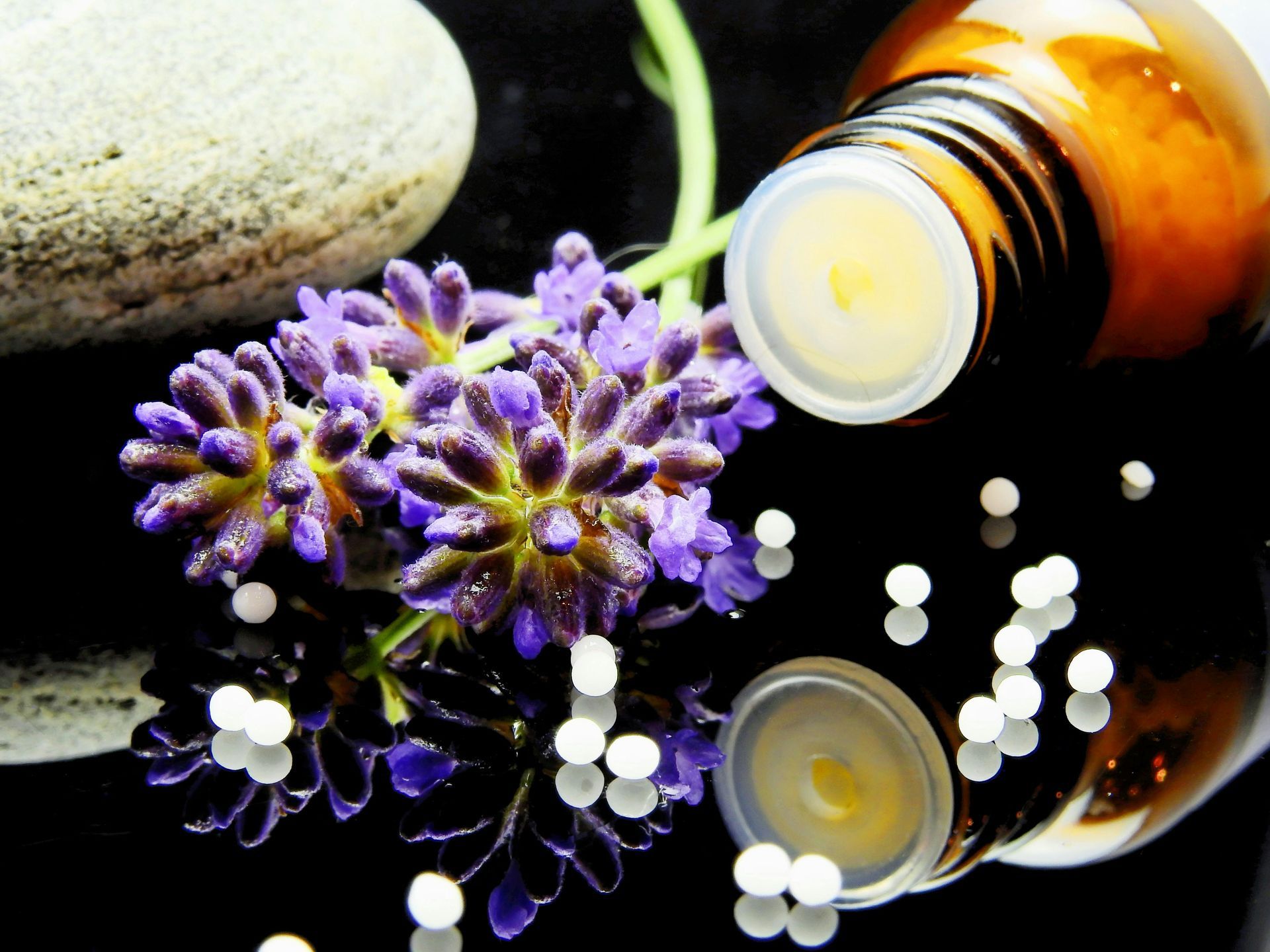 esential oil bottle laying on its side beside purple budding flower