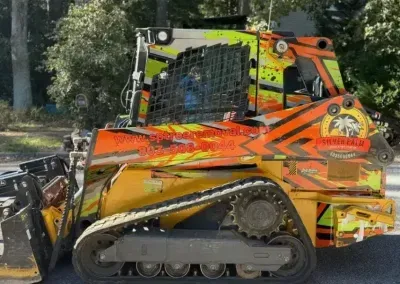 A bright yellow and orange tracked skid steer loader with custom graphic decals parked on pavement outdoors.