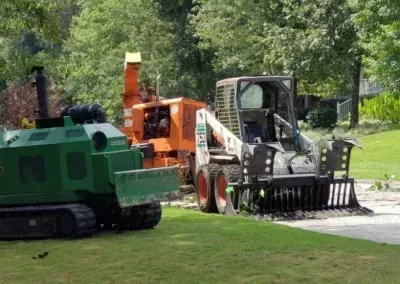 A green tracked machine, an orange wood chipper, and a white skid-steer loader parked on a lawn.