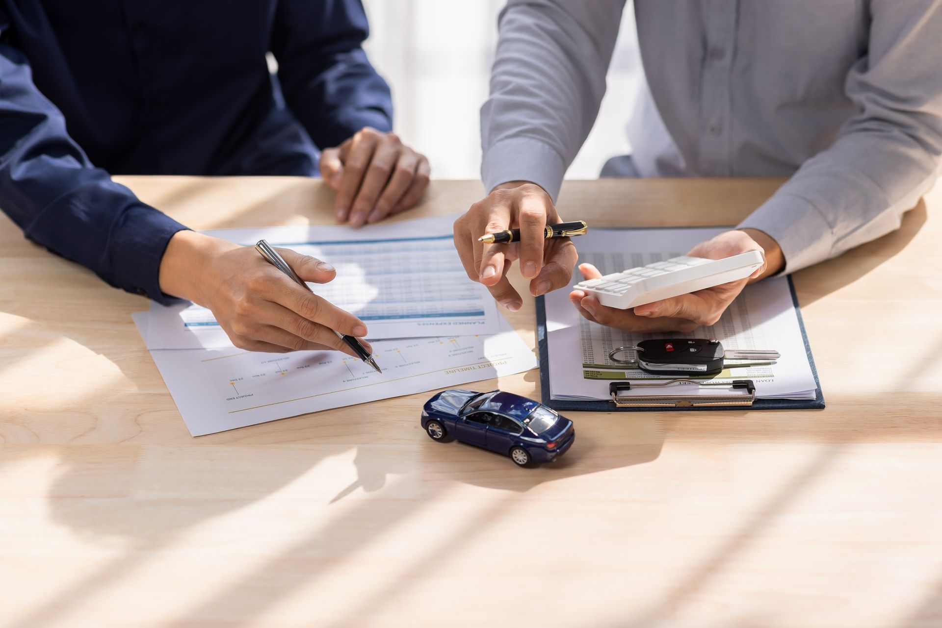 Two people reviewing paperwork with a calculator and toy car on a desk.