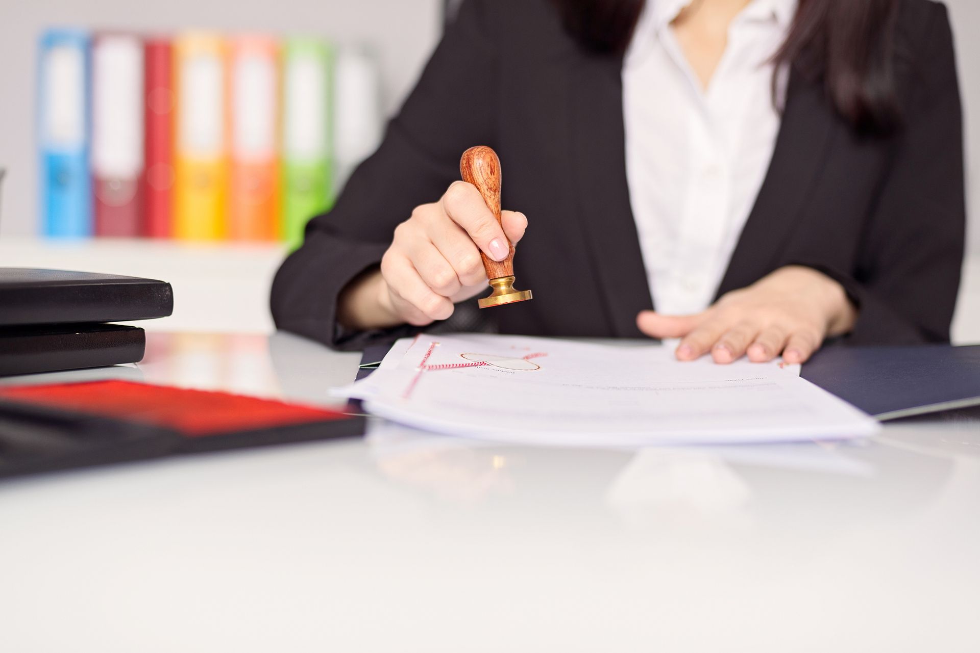 Woman in suit stamping document with a wax seal at a desk in an office setting.