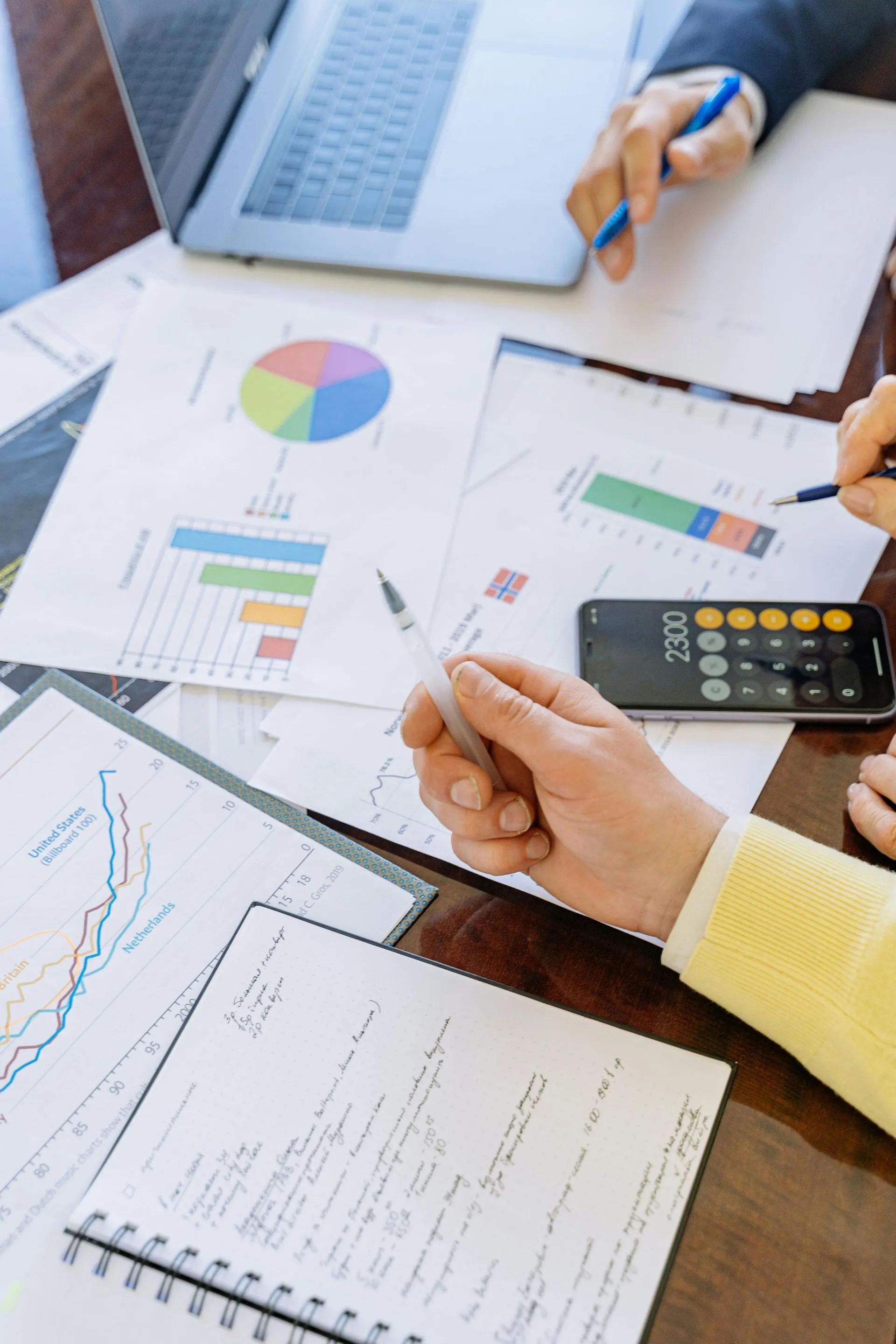 People reviewing financial documents with a laptop, charts, calculator, and notes on a wooden table.