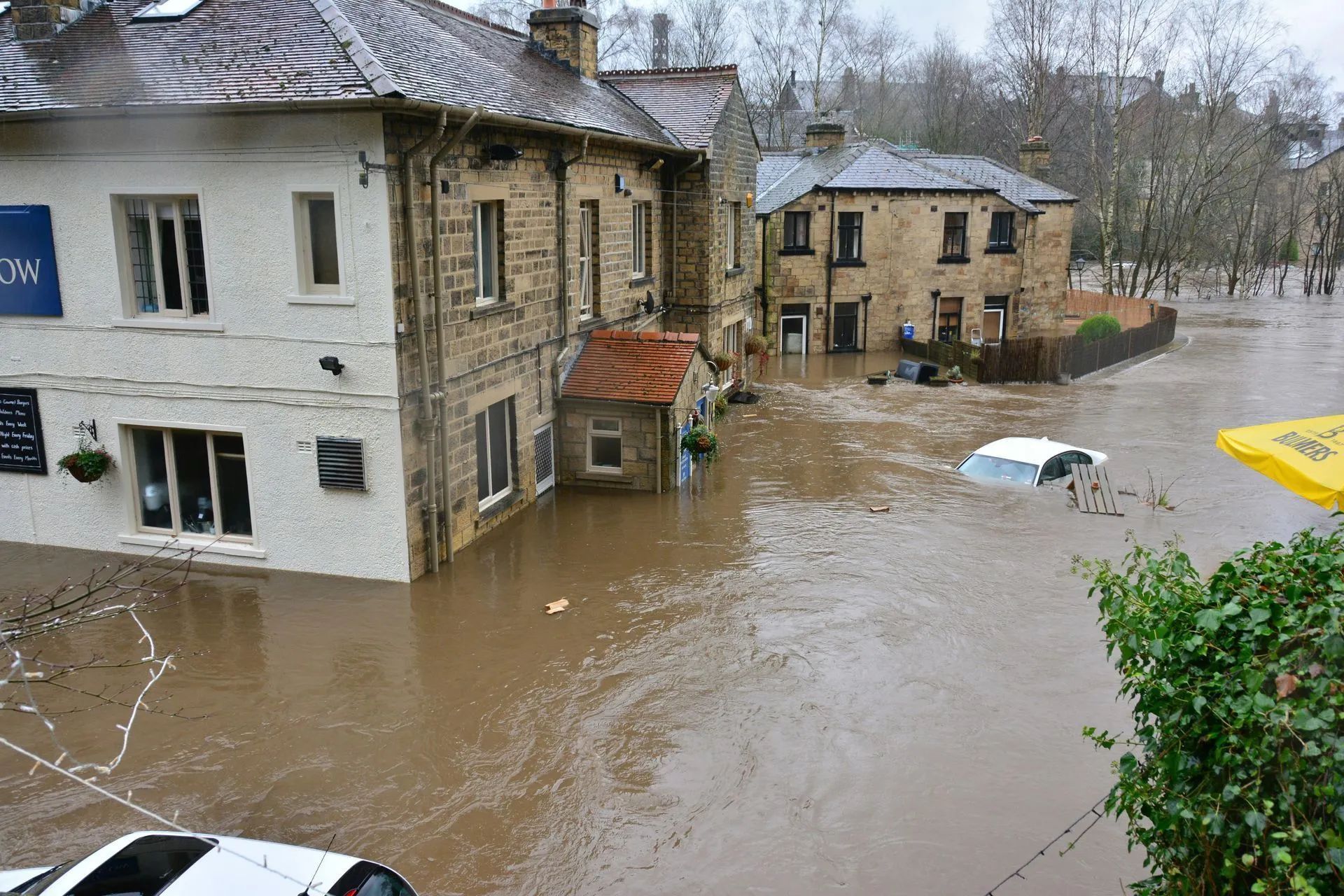 Flooded street with buildings and submerged cars; brown water.