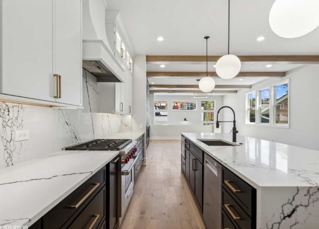 Bright modern kitchen with white cabinets, marble countertops, black island, and pendant lights