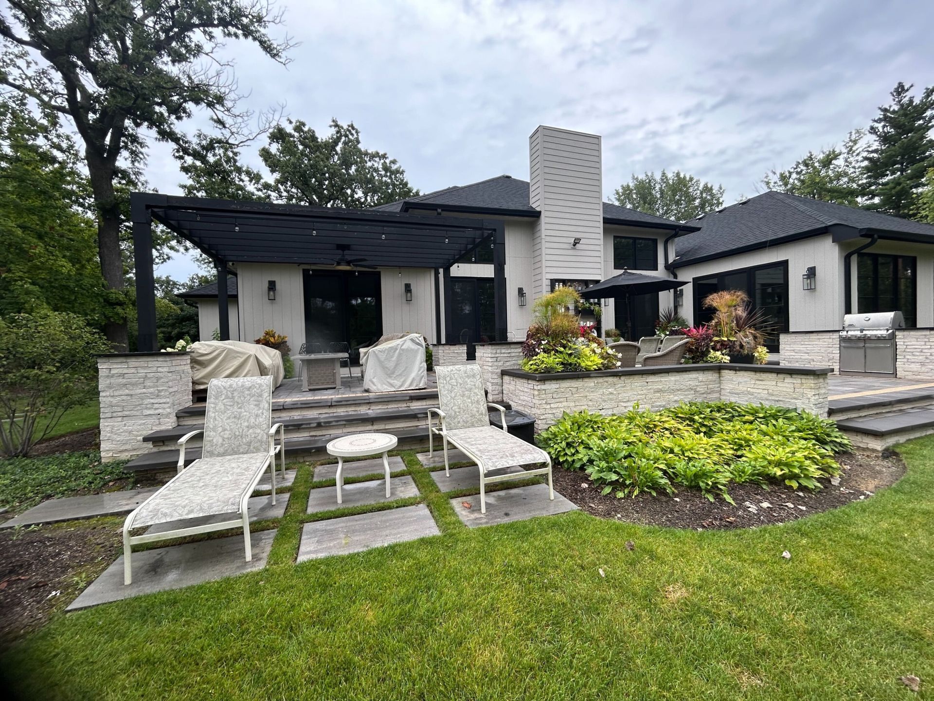 Backyard patio with lounge chairs, a white house, and green lawn.