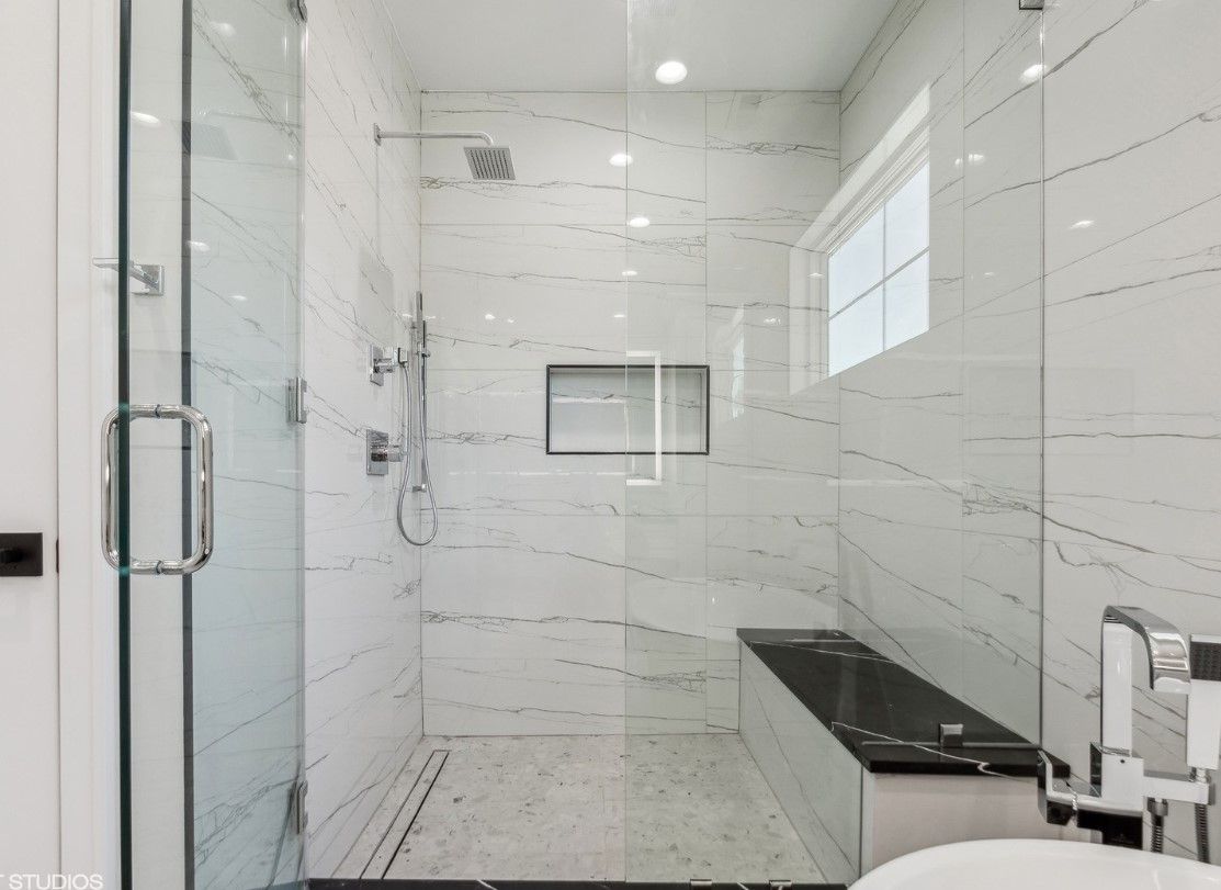Modern white-tiled shower with glass door, built-in niche, and bench seat