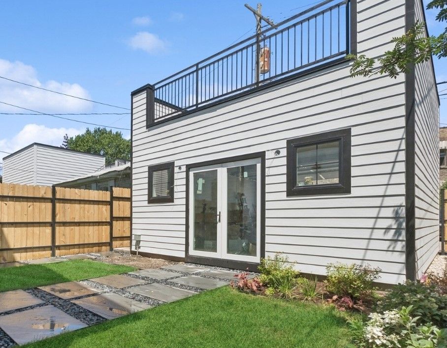 Modern white two-story house with rooftop deck, sliding glass doors, patio pavers, and small lawn
