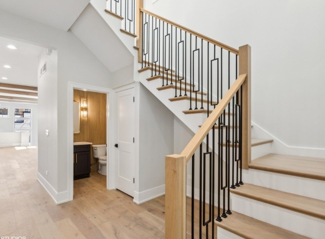 Bright entryway with white staircase, wood steps, and black railing beside a hallway opening