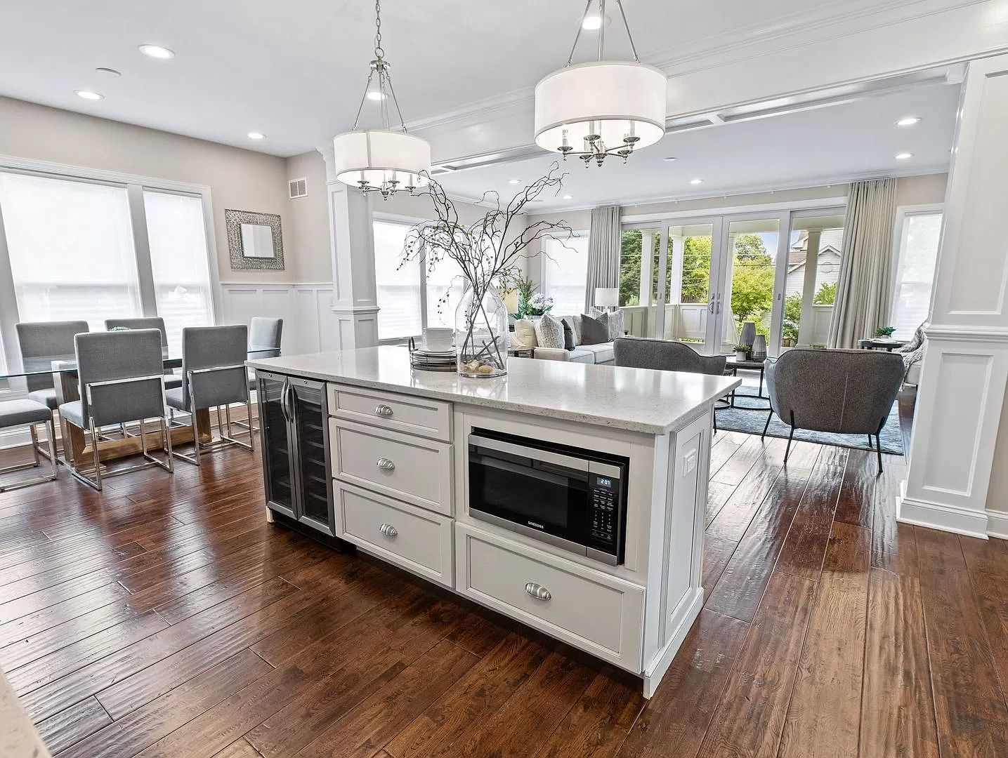 Kitchen with island, dining area, and living room visible. White cabinetry, wood floors, and bright lighting.