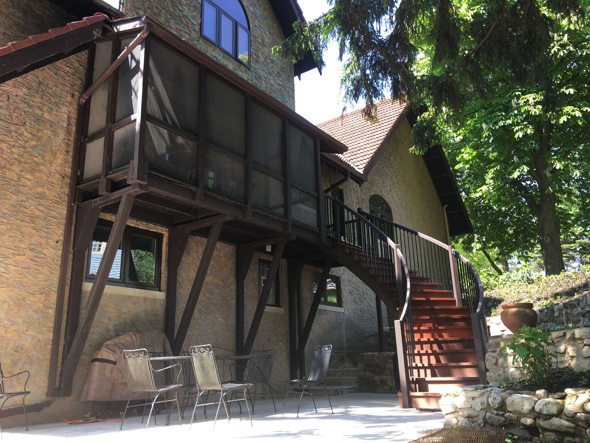 Stone building with screened porch, wooden staircase, and patio with chairs.