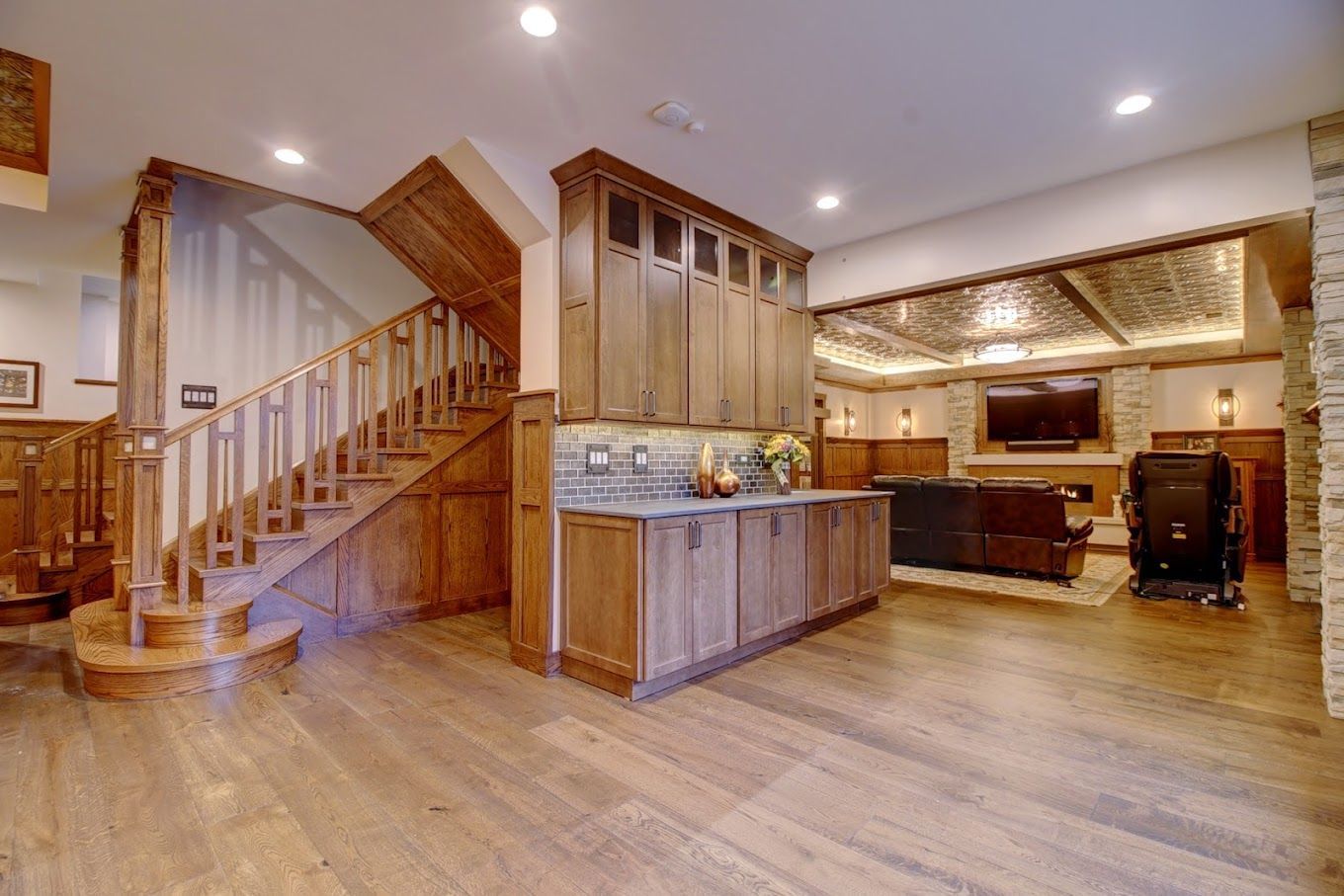 Spacious open-concept kitchen and living area with wooden floors, staircase, and warm recessed lighting