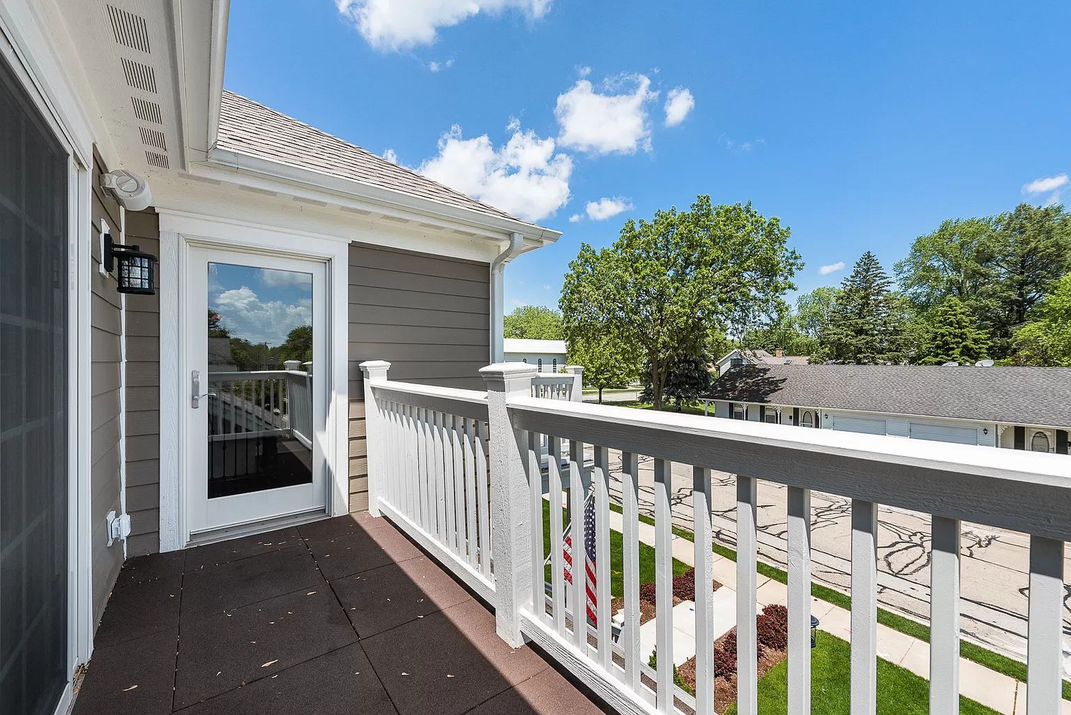 Balcony with white railing, glass door, and view of houses on a sunny day.