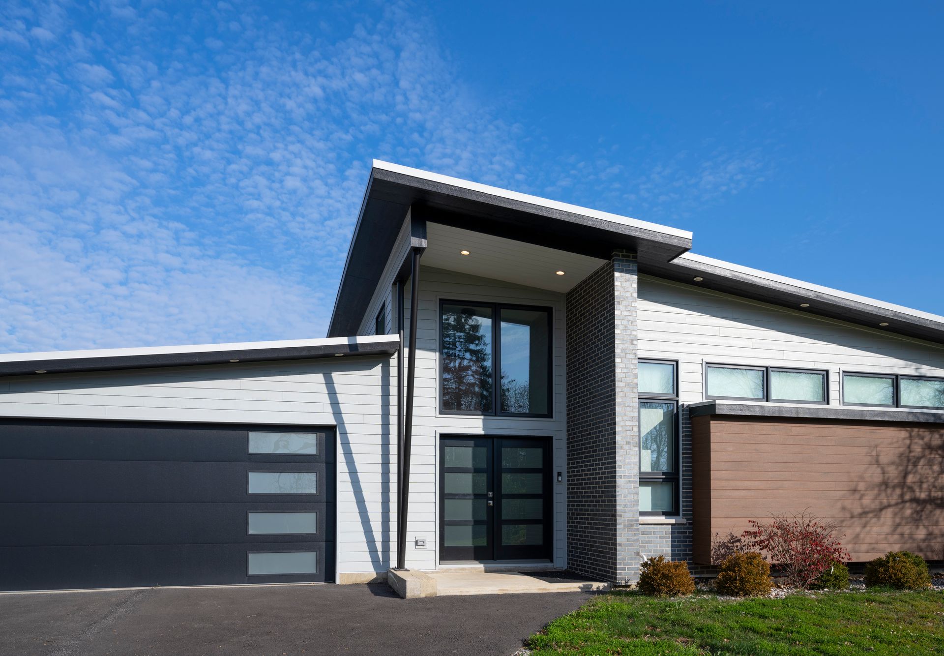 A modern house with a black garage door and a blue sky in the background.