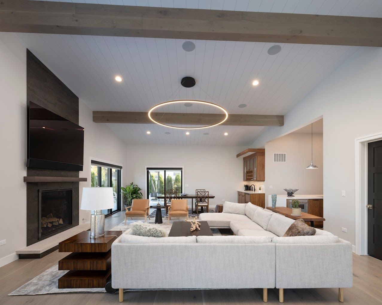Modern open-plan living room with sectional sofa, fireplace, dining area, and large circular ceiling light