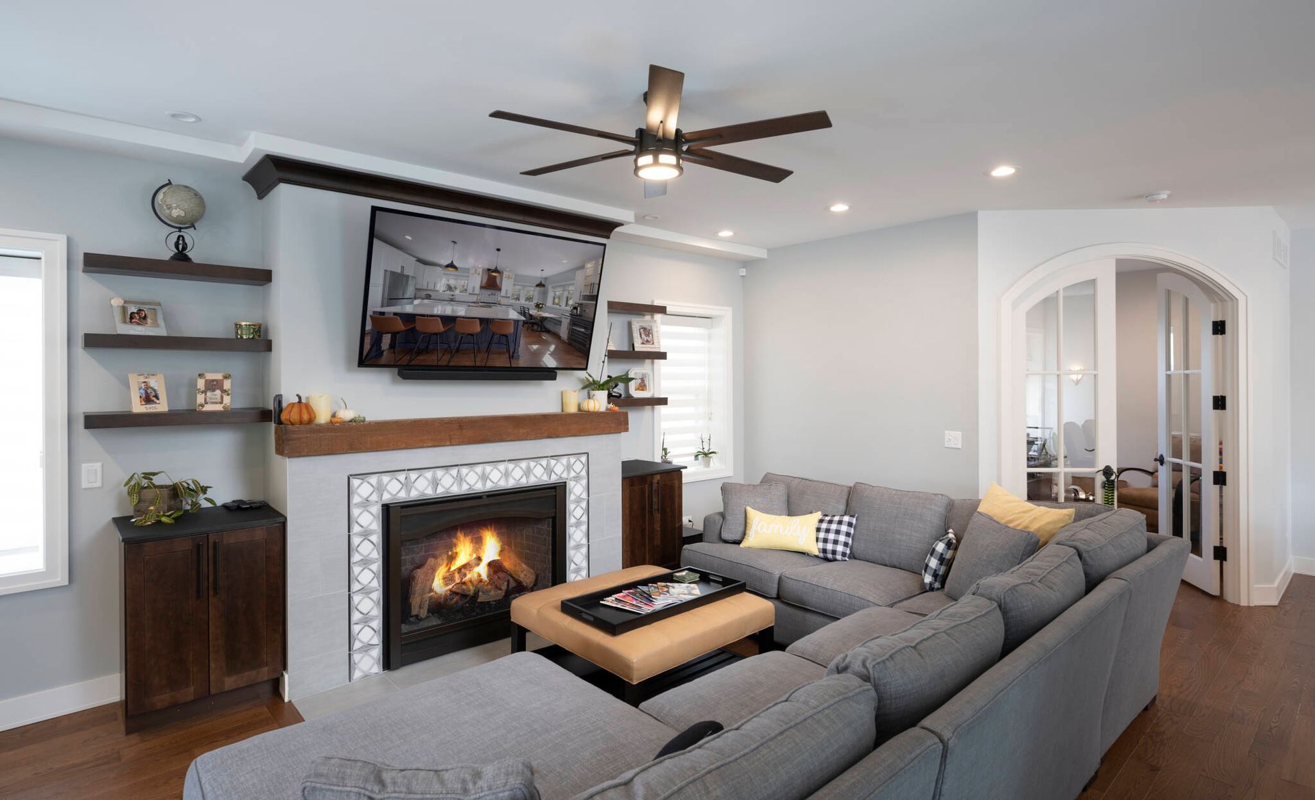 Living room with gray sectional, fireplace, mounted TV, floating shelves, and arched doorway.