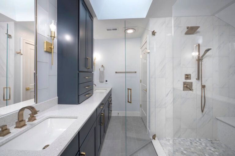 A bathroom with a walk in shower , sink , mirror and cabinets.