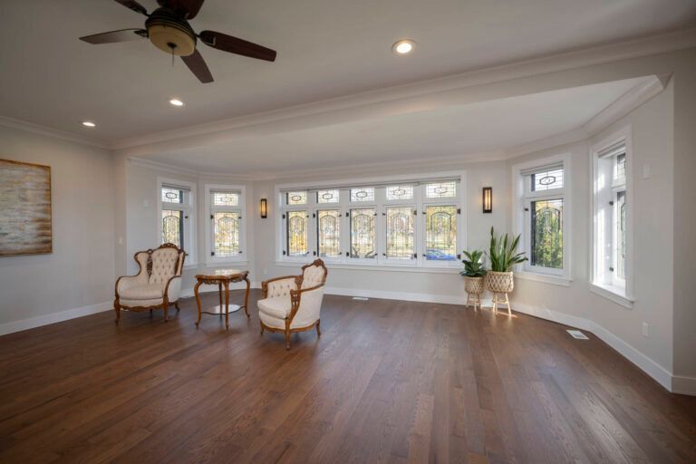 A living room with hardwood floors , chairs , a table and a ceiling fan.