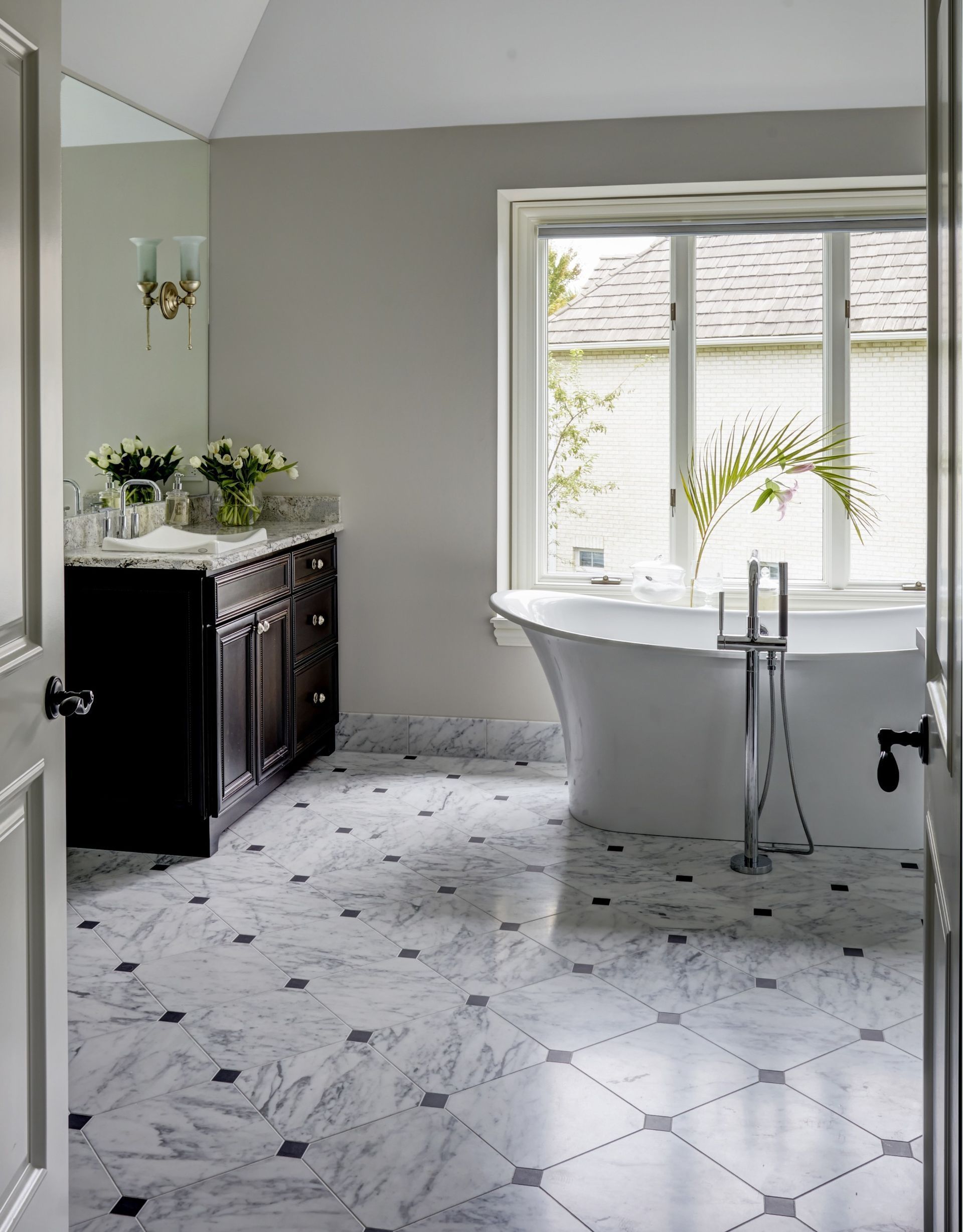 A bathroom with a tub , sink , mirror and window.