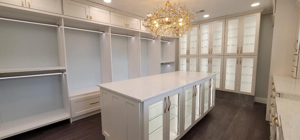 A walk in closet with a large island in the middle and a chandelier hanging from the ceiling.