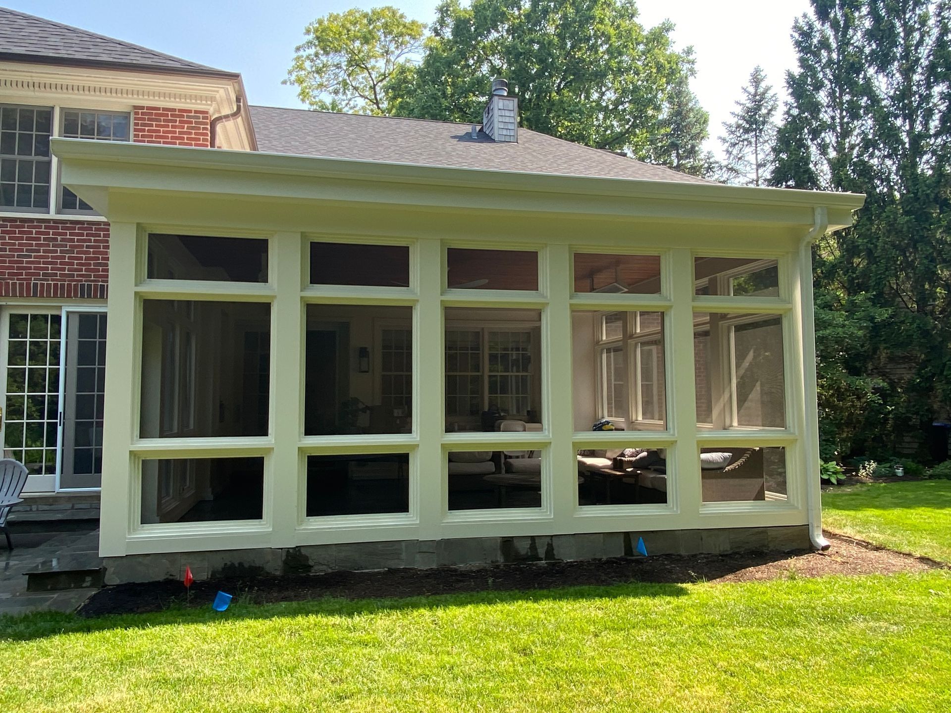 A screened in porch with lots of windows is in the backyard of a house.