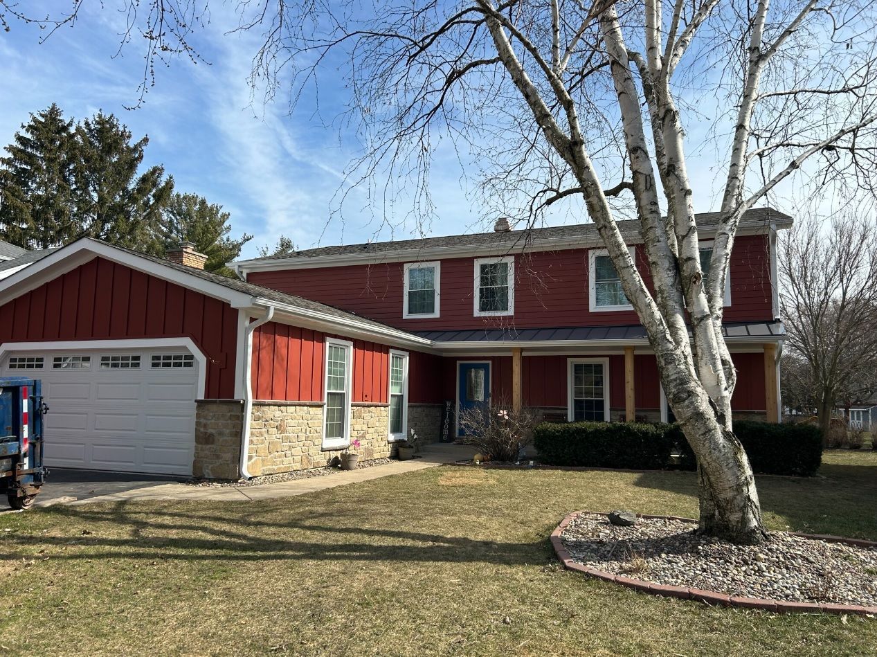A red house with a white garage door and a tree in front of it.