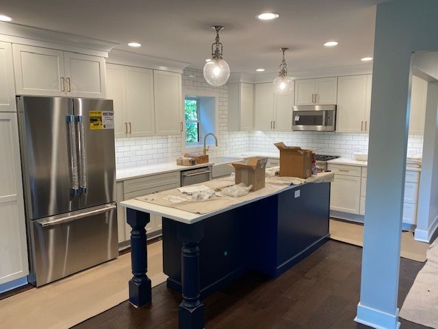 A kitchen with white cabinets , stainless steel appliances , and a blue island.