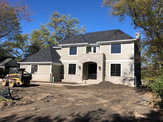 A large house is being built with a bulldozer in front of it.