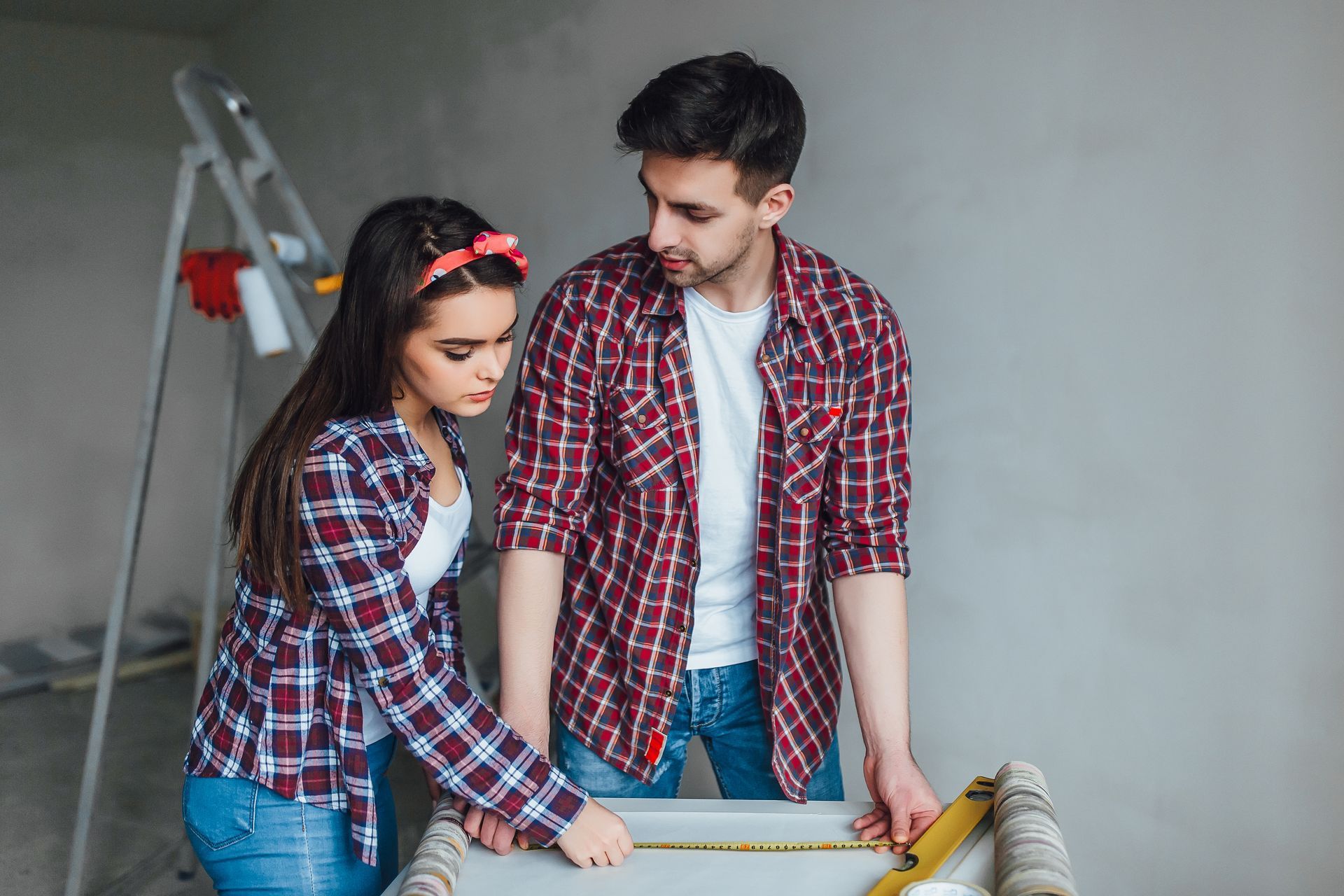 A man and a woman are measuring a wall with a tape measure.