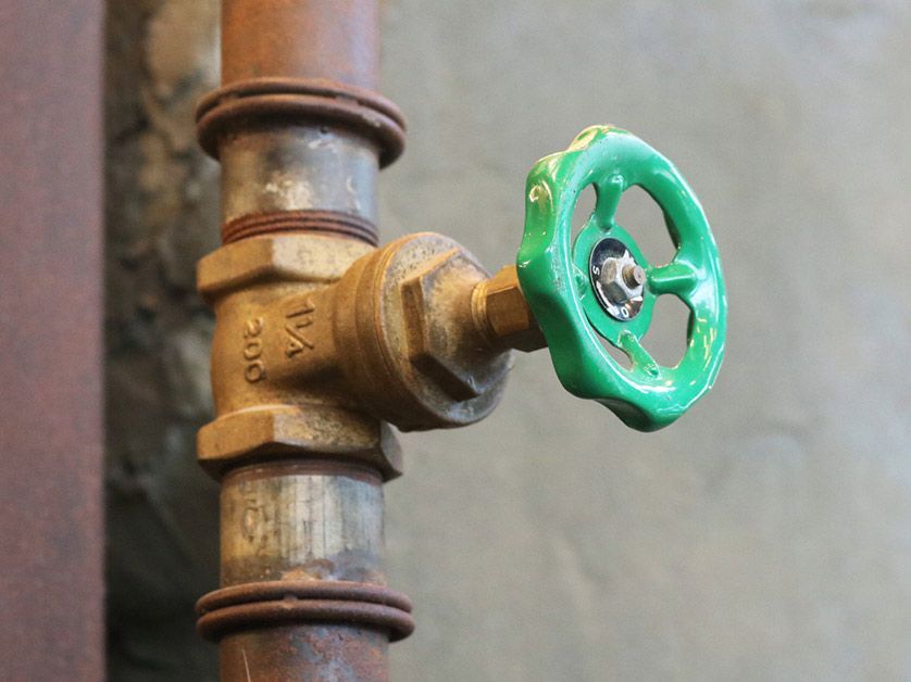 A green valve is attached to a rusty pipe.