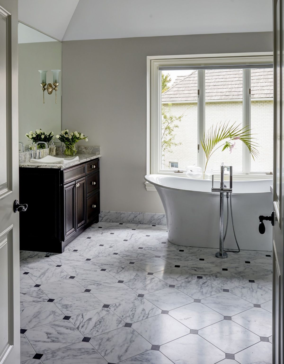 A bathroom with a tub , sink , mirror and window.
