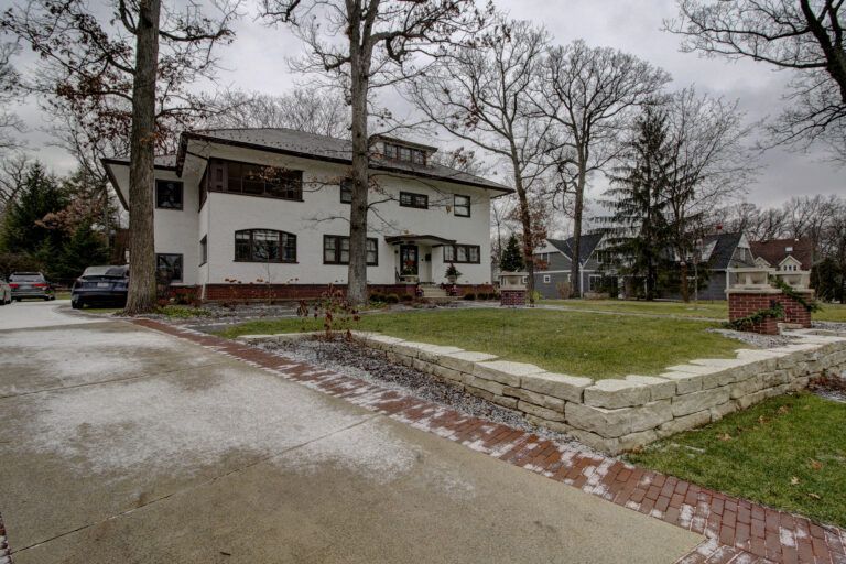 A large white house with a brick driveway and a car parked in front of it.