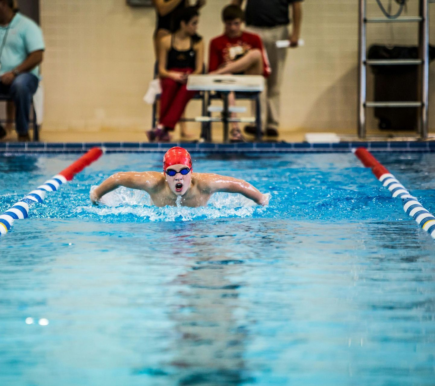 A man is swimming in a swimming pool while people watch.