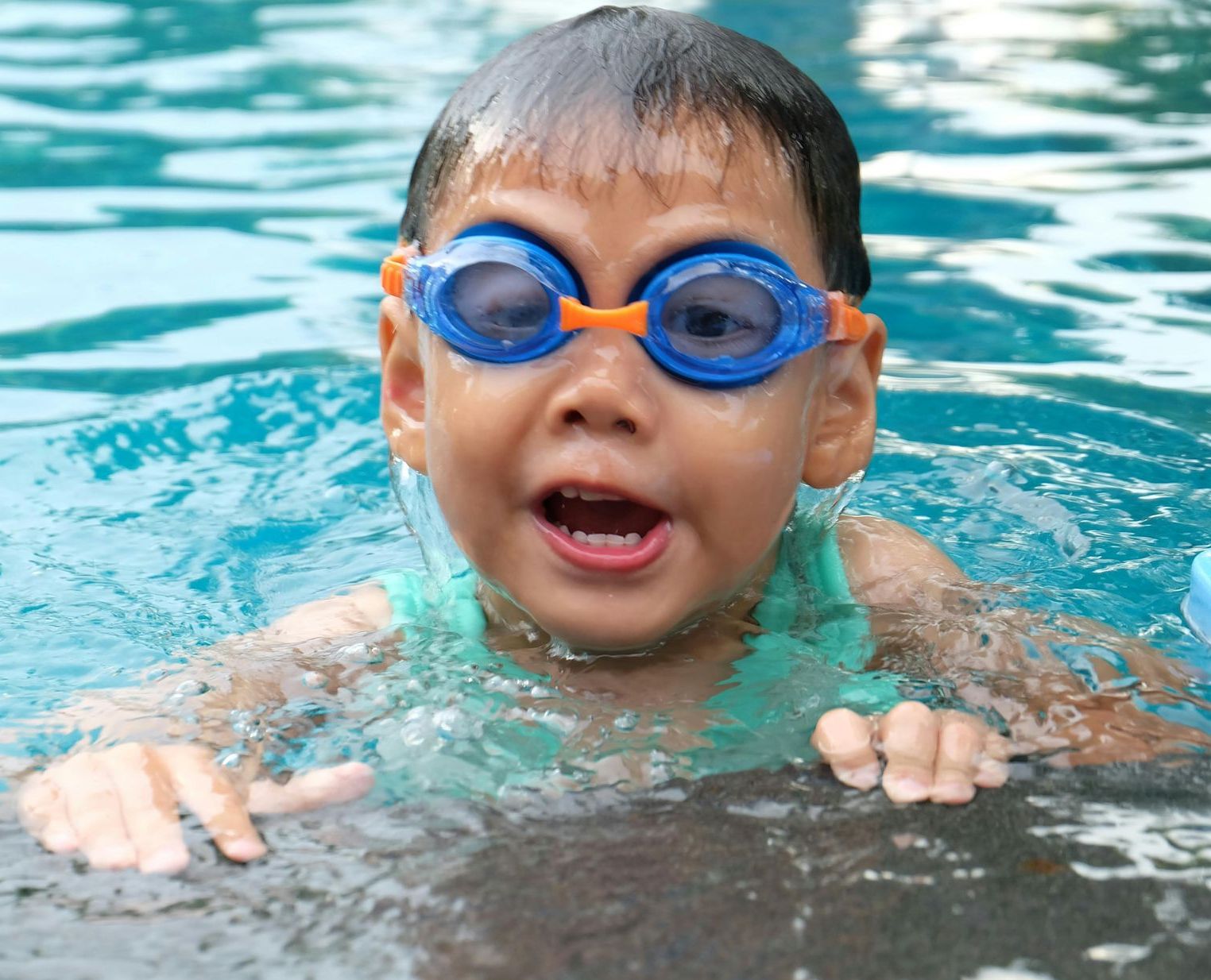 A young boy wearing goggles is swimming in a pool.