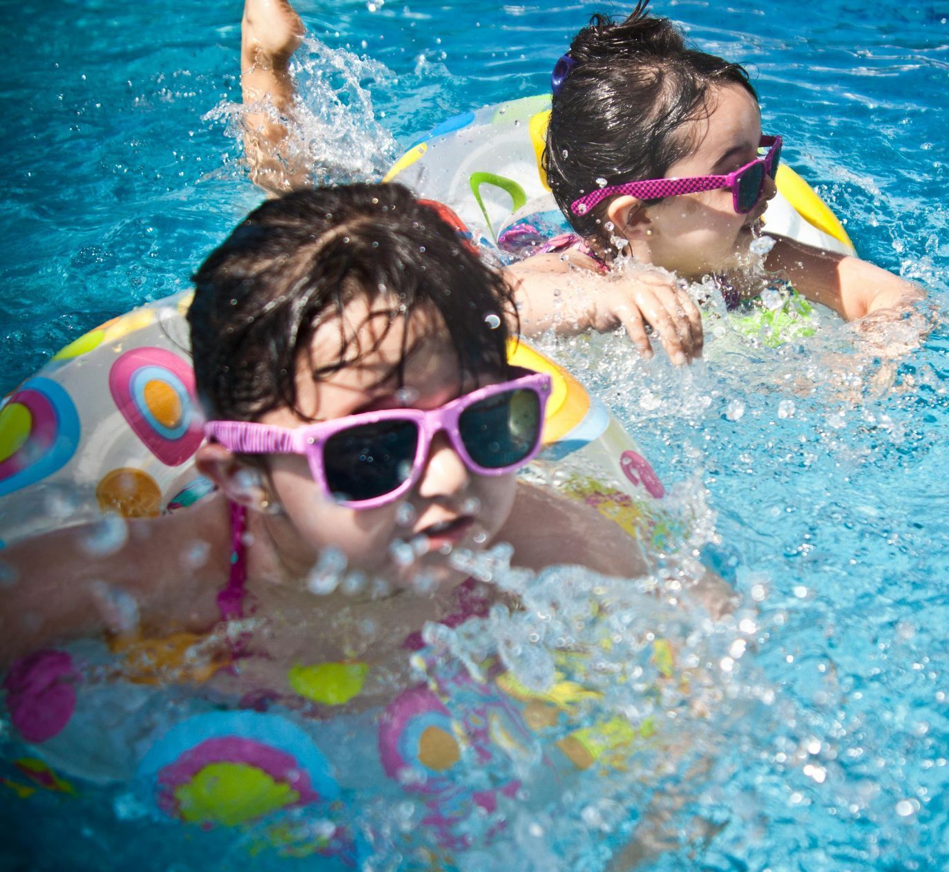 Two little girls wearing sunglasses are swimming in a pool