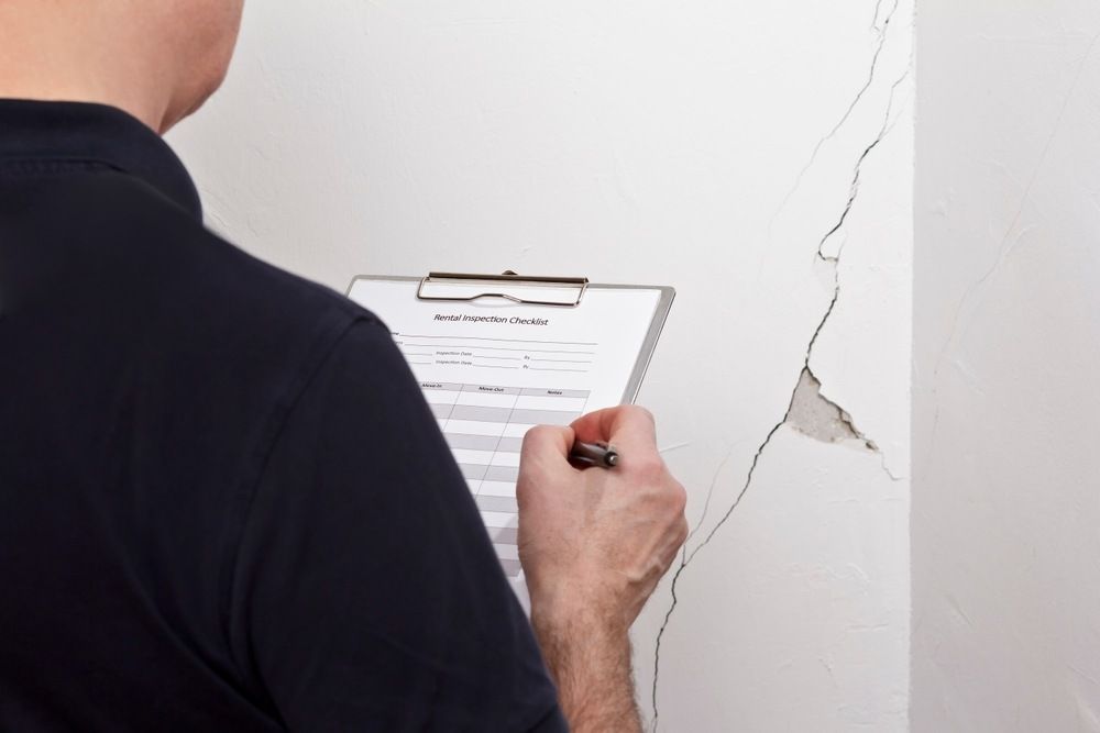 Man with inspection checklist looking at a cracked basement wall. 