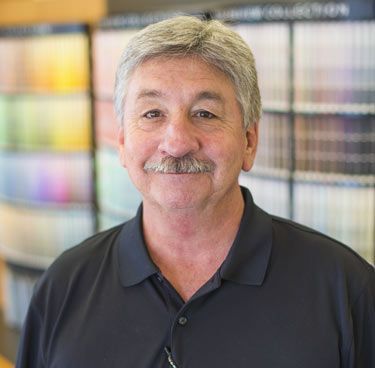 A man with a mustache is standing in front of a wall of paint.