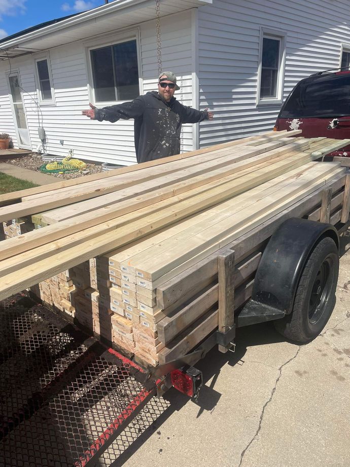 A man is standing next to a trailer filled with wood.