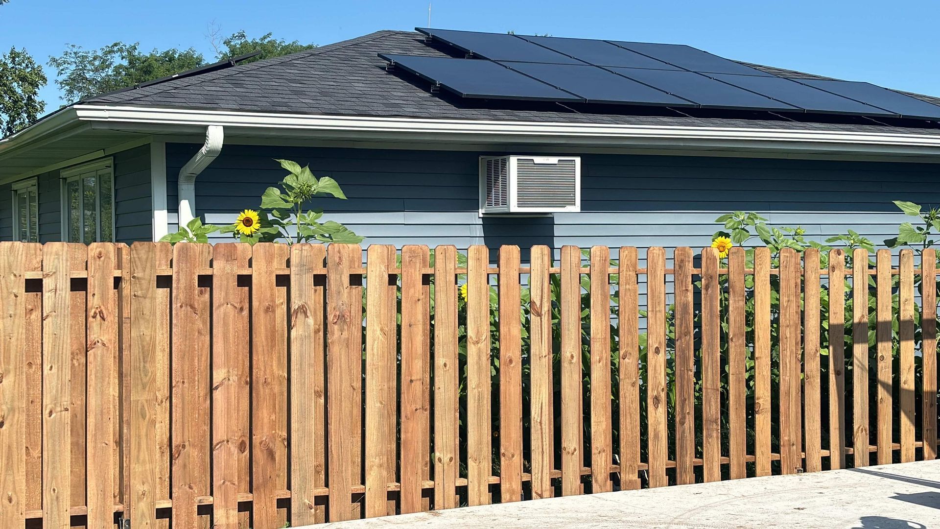 A wooden fence surrounds a house with solar panels on the roof.