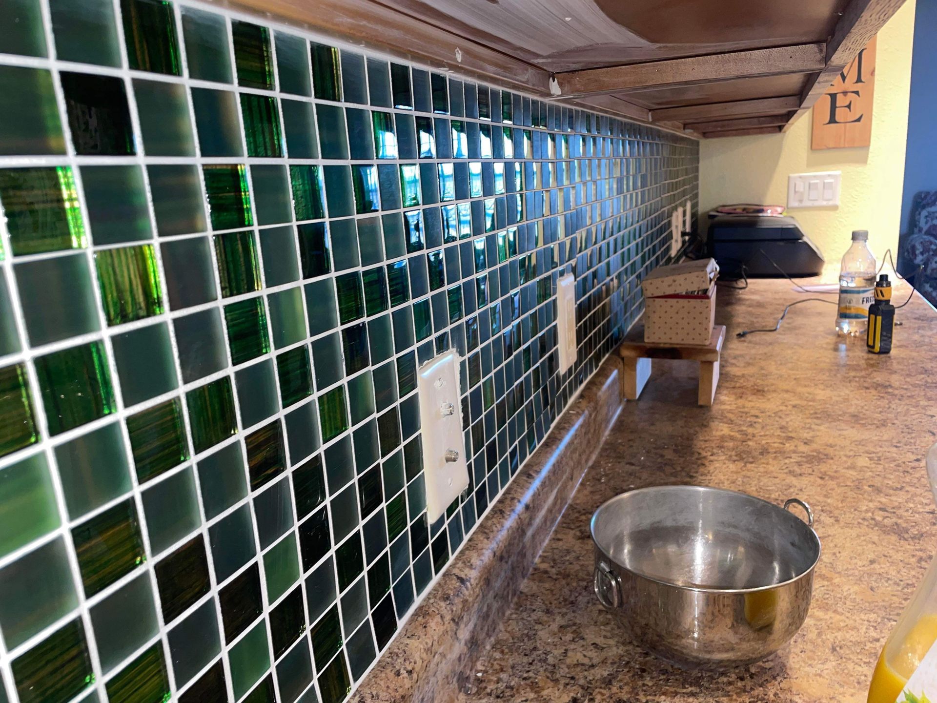 A kitchen with green tiles and a stainless steel bowl on the counter.
