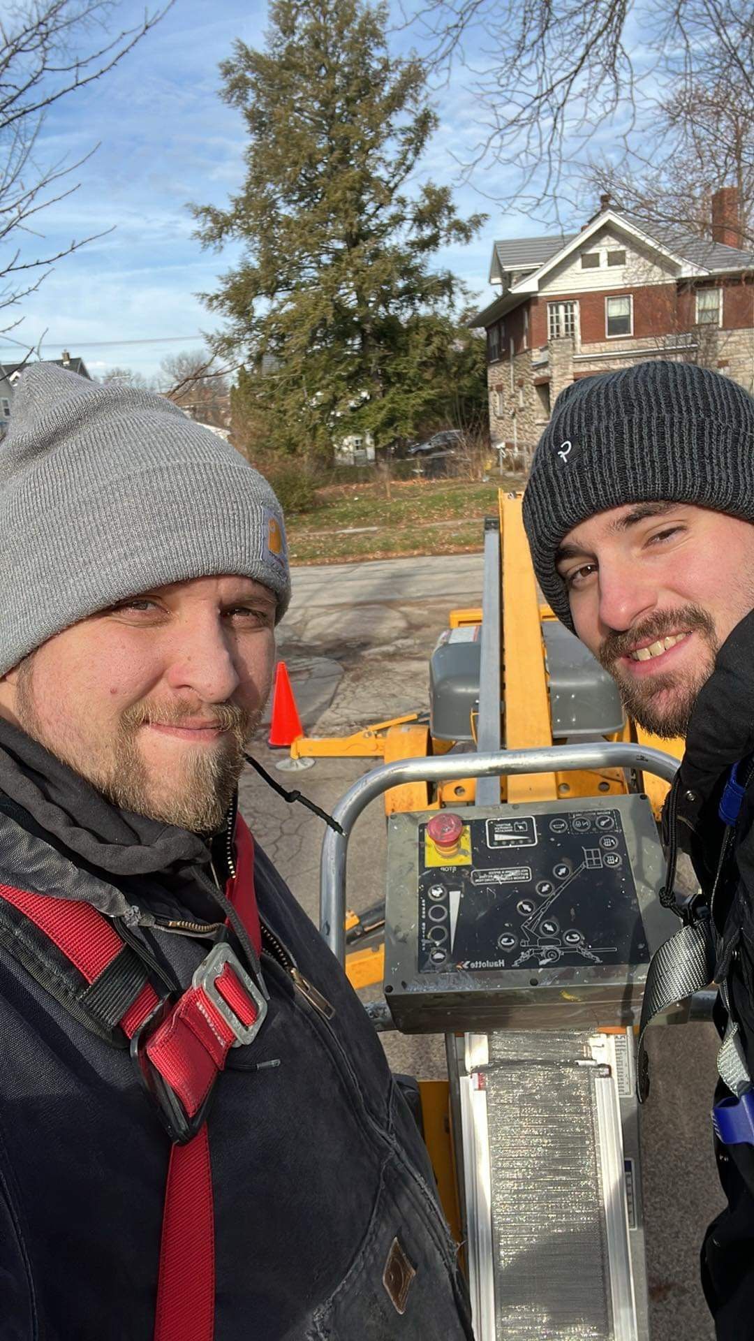 Two men are standing next to each other in front of a tree.