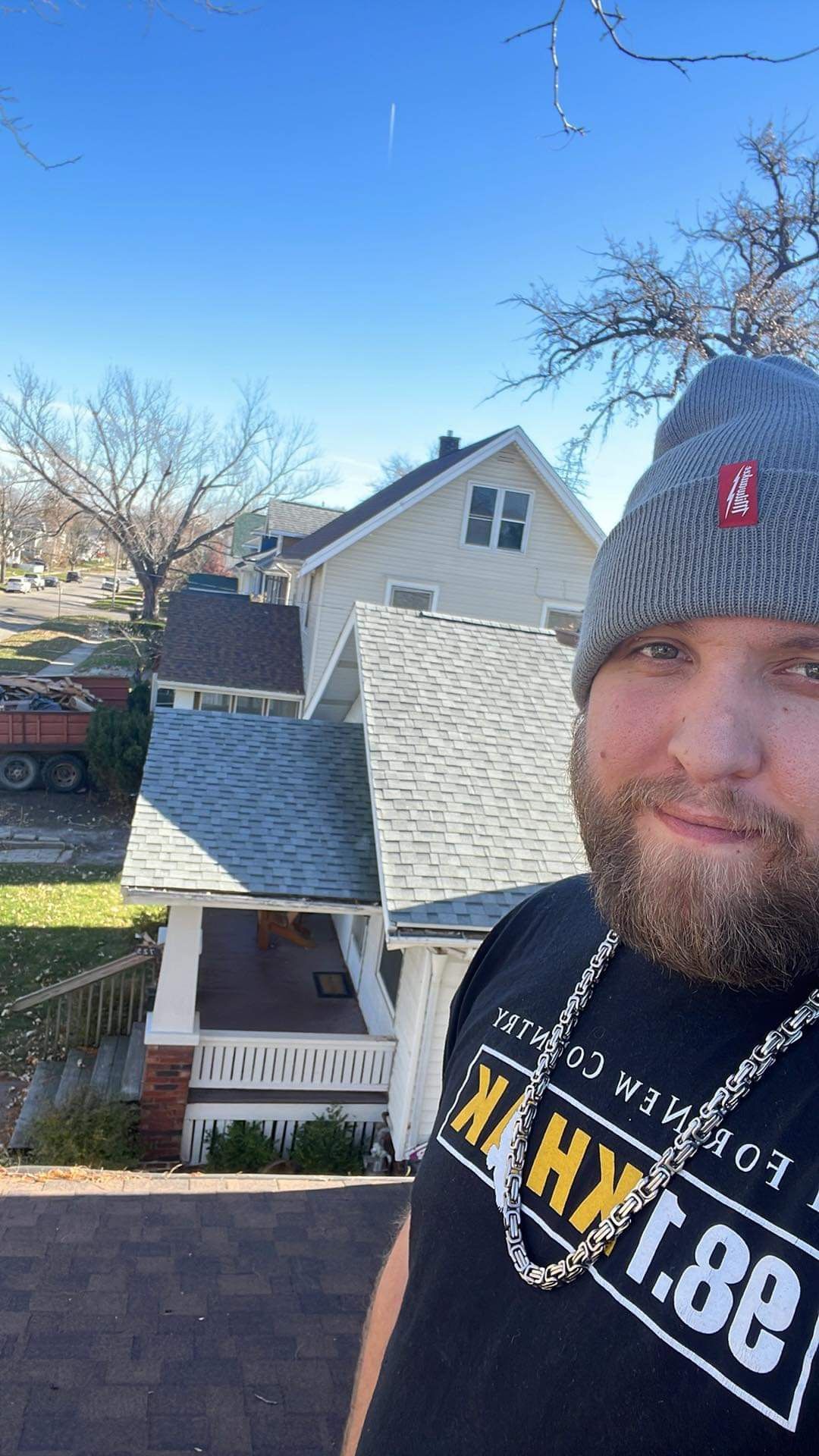 A man wearing a beanie and a necklace is standing in front of a house.