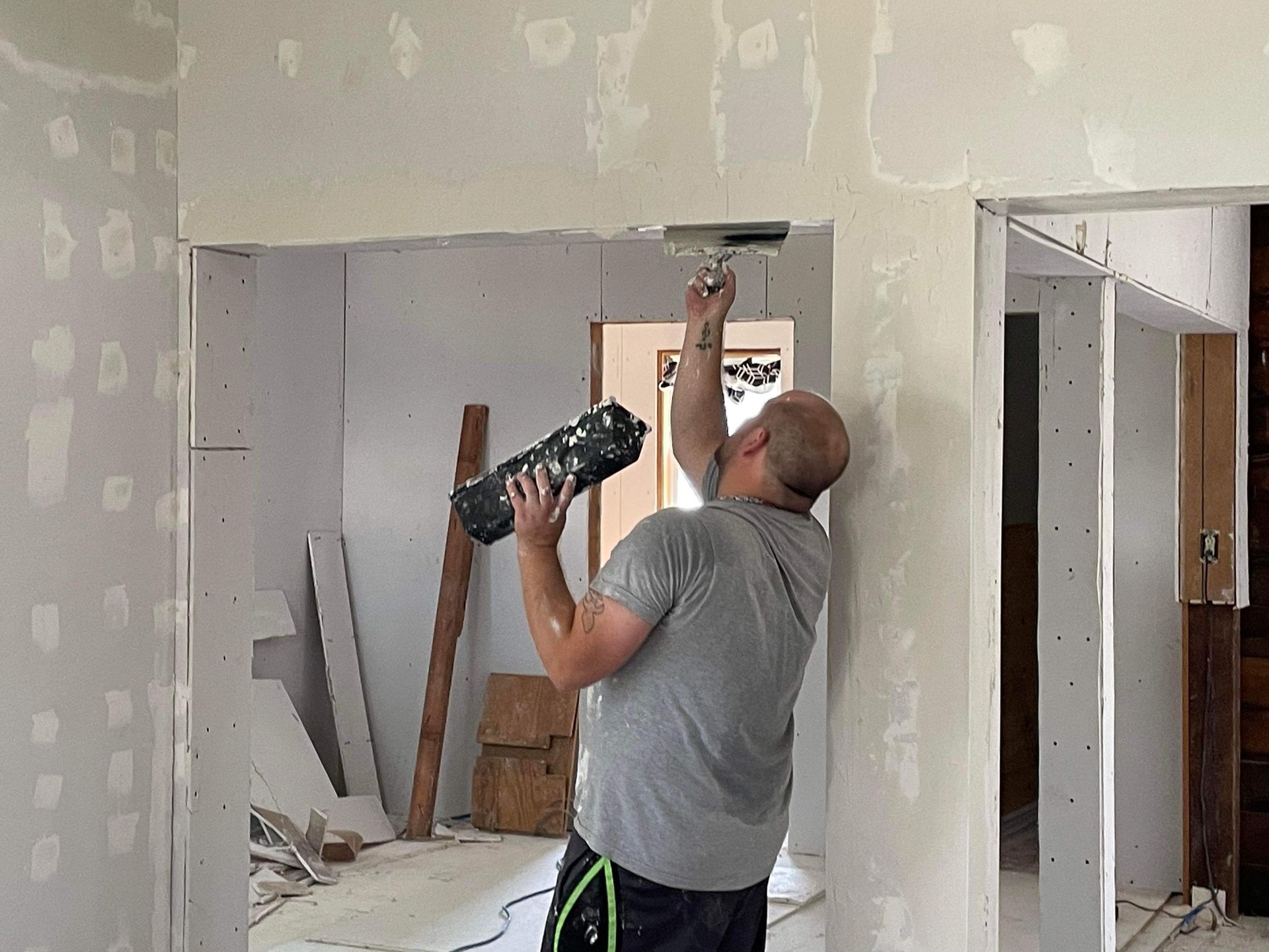 A man is working on a wall in a room while holding a camera.