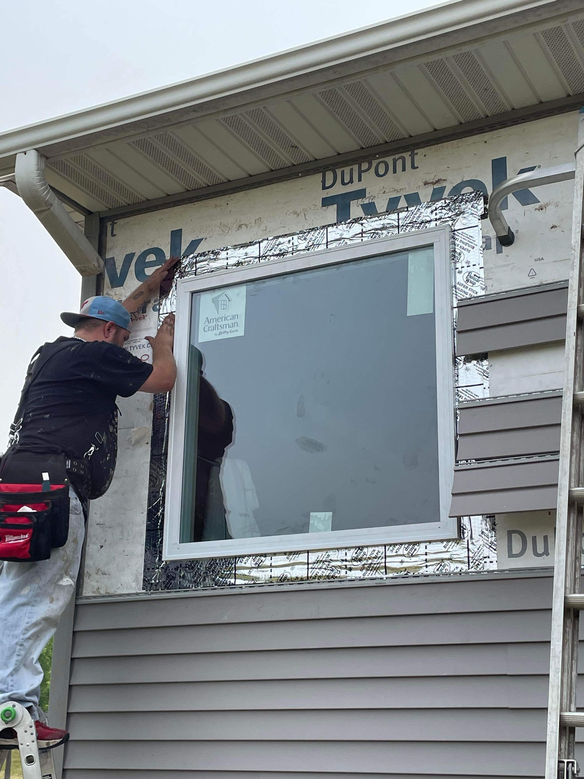 A man is installing a window on the side of a house.