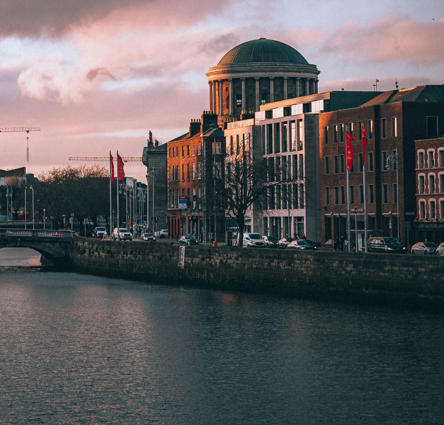 River Liffey in Dublin, Ireland. Buildings line the riverbank, including a domed courthouse. Cloudy sky reflects in water.