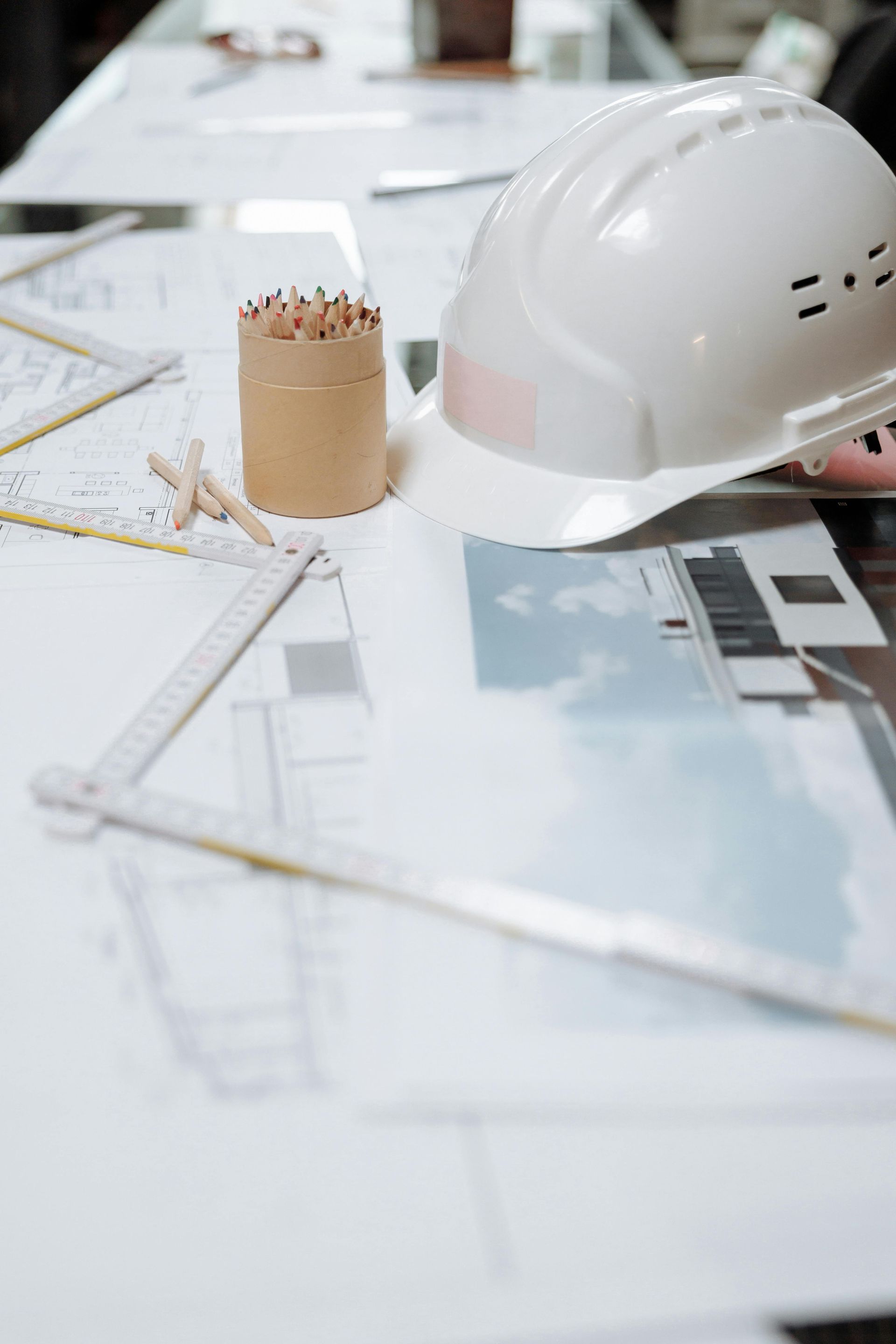 White hard hat, pencils, and blueprints on a table, likely in an architect's or engineer's workspace.