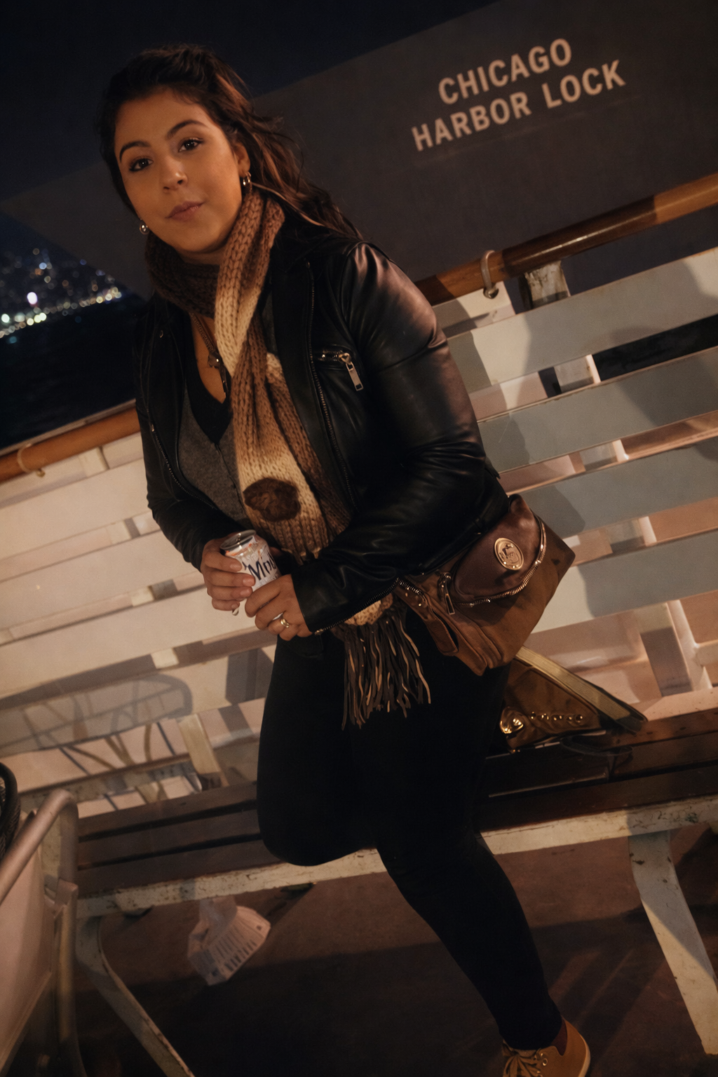 Woman in a black jacket leaning on a bench at Chicago Harbor Lock at night.