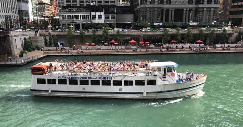 Tour boat packed with passengers cruising on a green river past a city waterfront